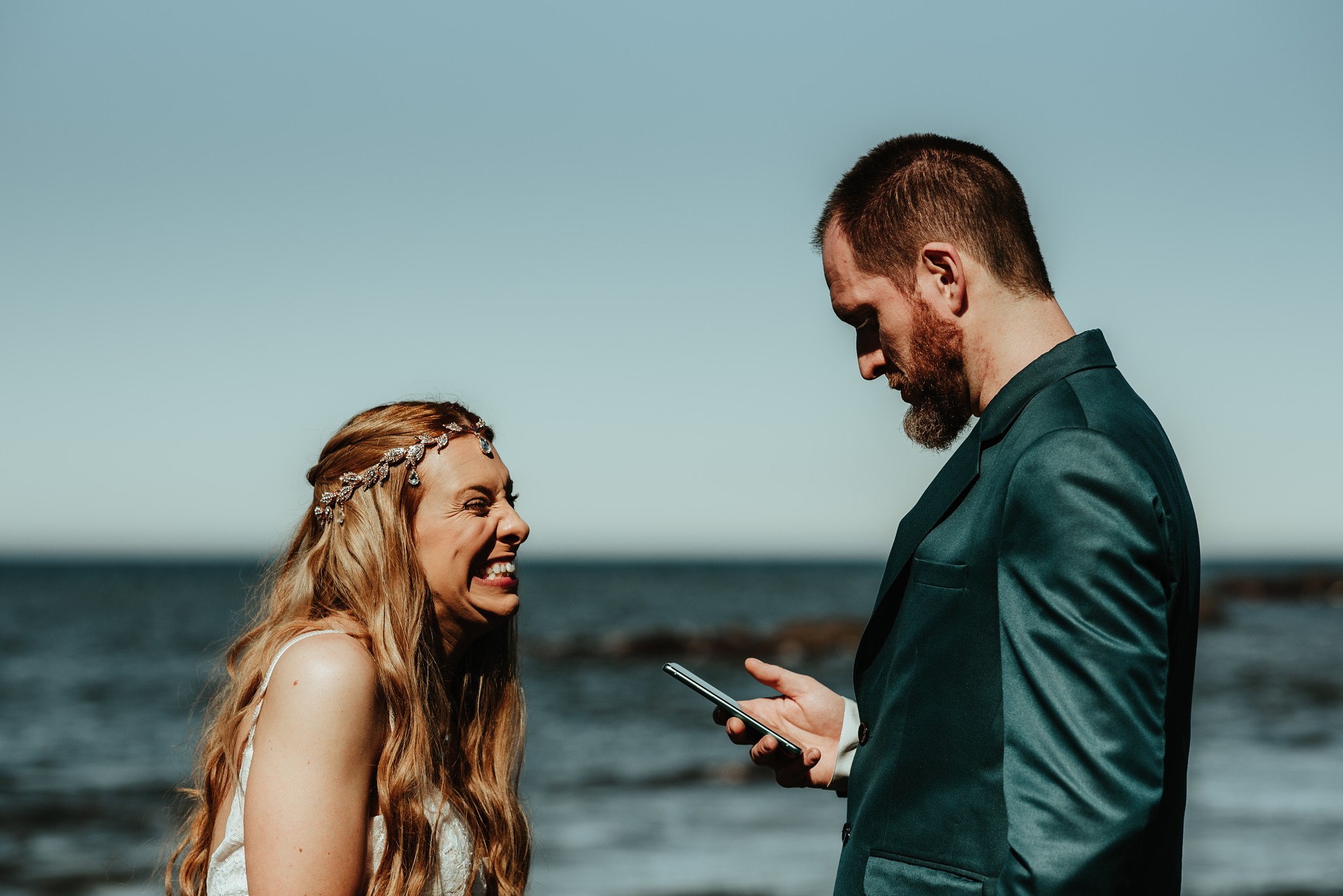 The bride is grinning wildly as the groom reads his vows.